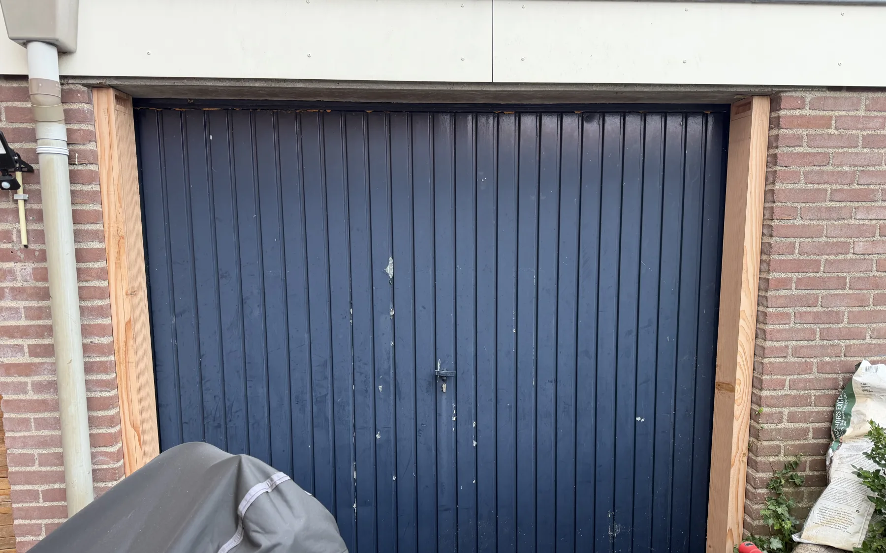 The old blue painted steel up-and-over door in the brick garage opening, with the new Douglas frame posts already standing beside it